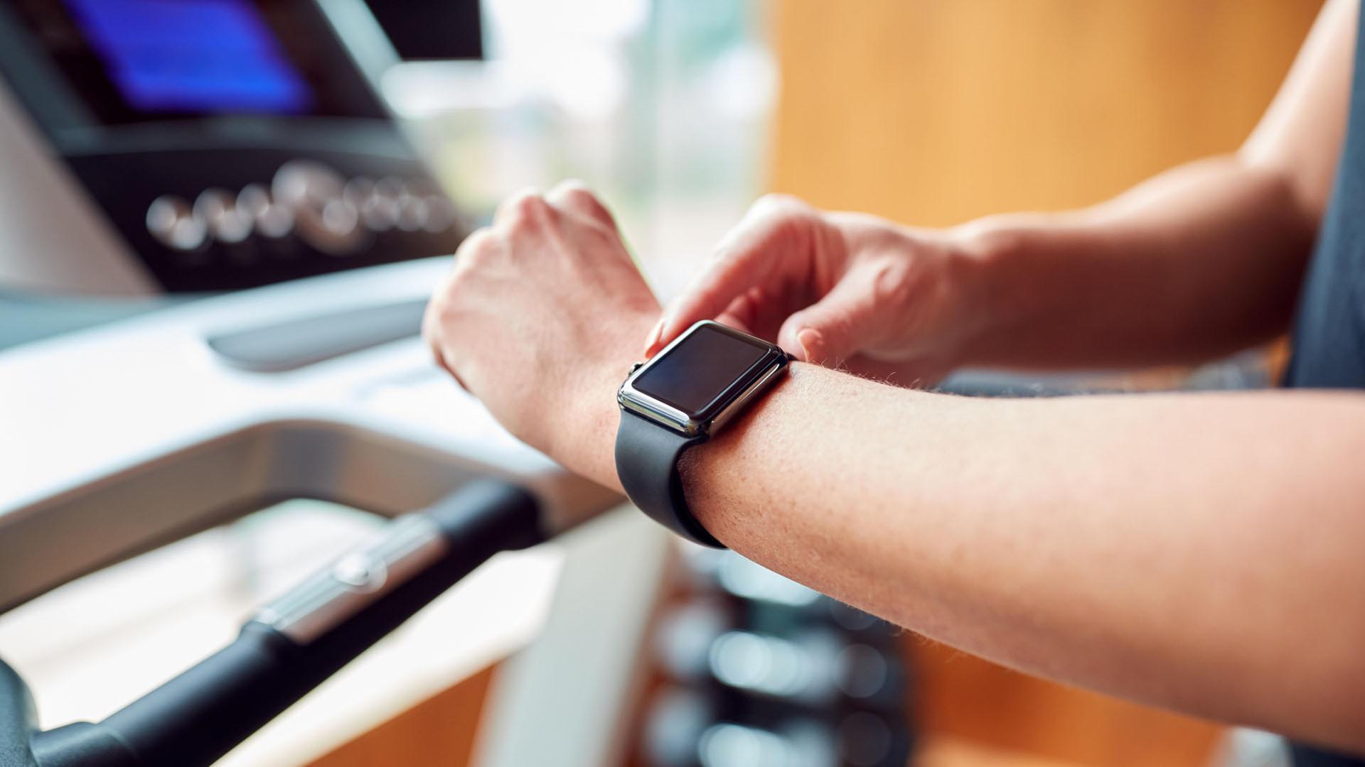 Eine Person auf einem Laufband bedient eine Smartwatch. | picture alliance / Shotshop