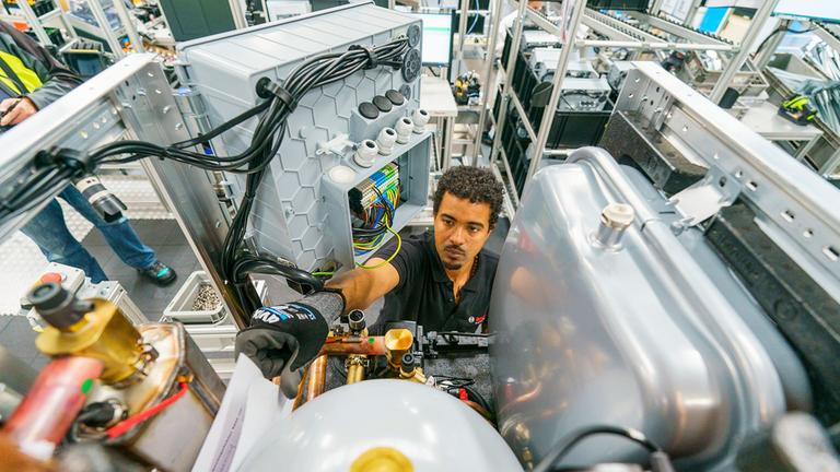 Ein Mitarbeiter arbeitet in der Montagestraße an einer Wärmepumpe. 