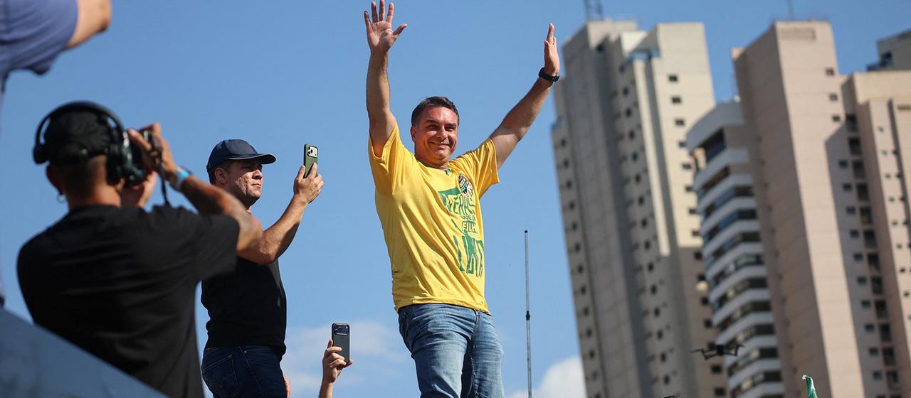 Flávio Bolsonaro steht erfreut auf einem Podest.