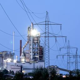 Strommasten stehen im Morgenlicht vor einem Zementwerk.