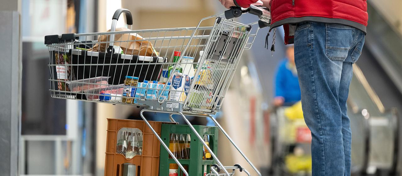 Ein Mann steht vor einem Supermarkt mit einem vollen Einkaufswagen.