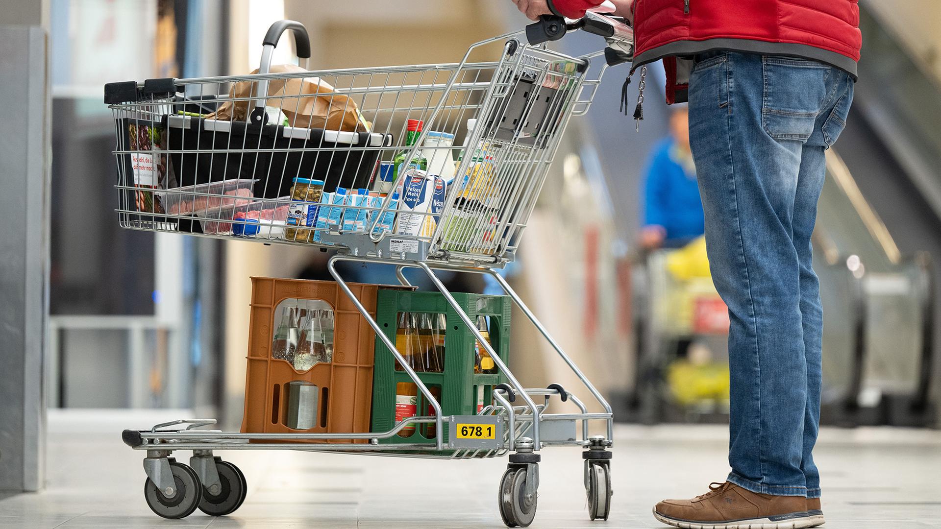 Ein Mann steht vor einem Supermarkt mit einem vollen Einkaufswagen. | dpa