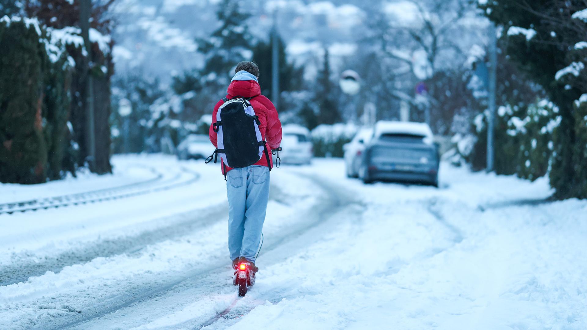 Ein junger Mann fährt mit einem E-Scooter auf mit Schnee bedeckter Straße. | dpa