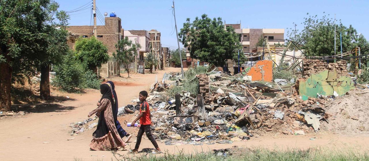 Menschen gehen in der Hauptstadt Khartum an den Trümmern eines Gebäudes vorbei.