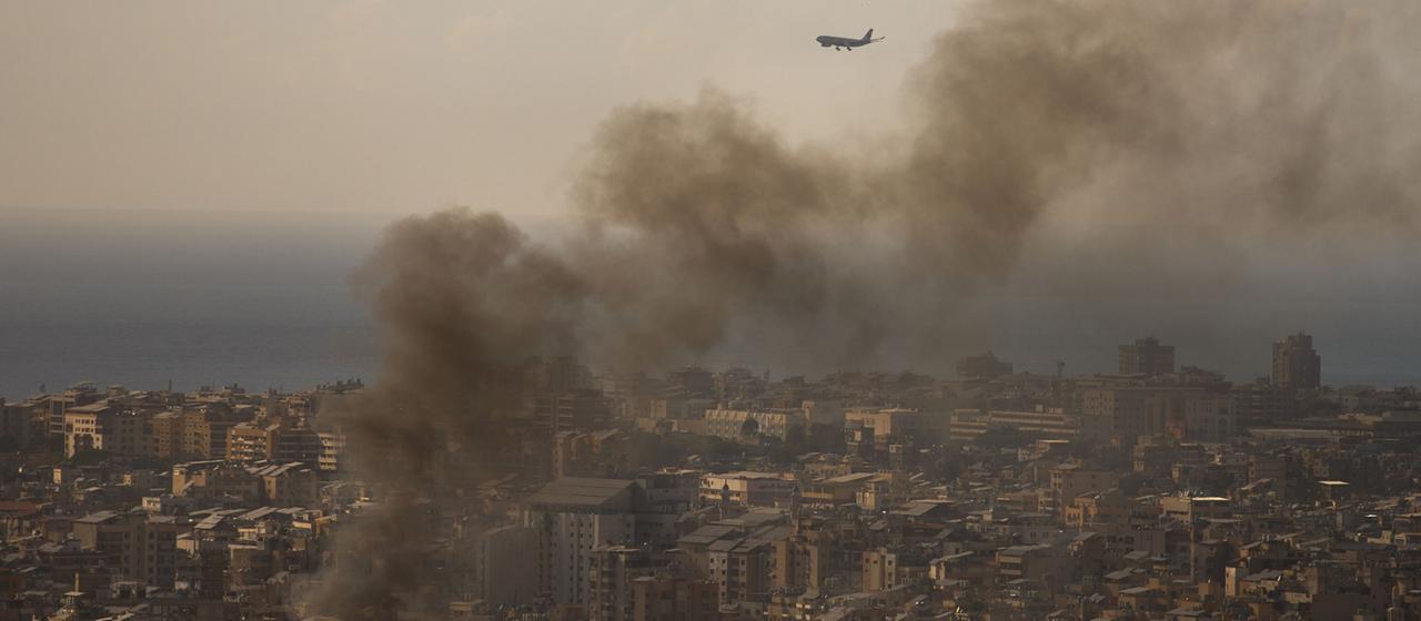 Ein Flugzeug im Landeanflug auf den Beiruter Flughafen - Rauchwolken im Vordergrund.