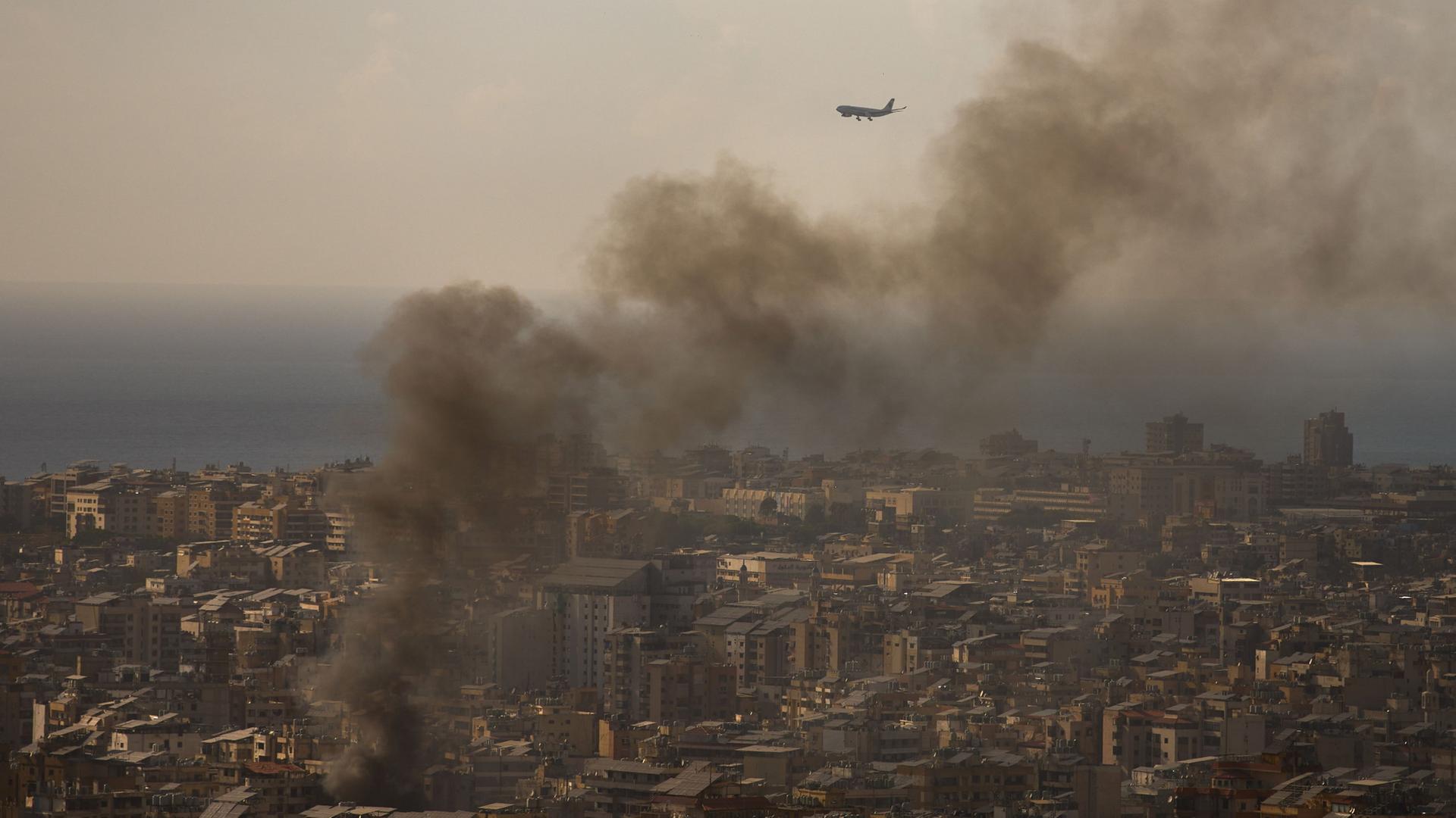 Ein Flugzeug im Landeanflug auf den Beiruter Flughafen - Rauchwolken im Vordergrund. | Emilio Morenatti/AP/dpa