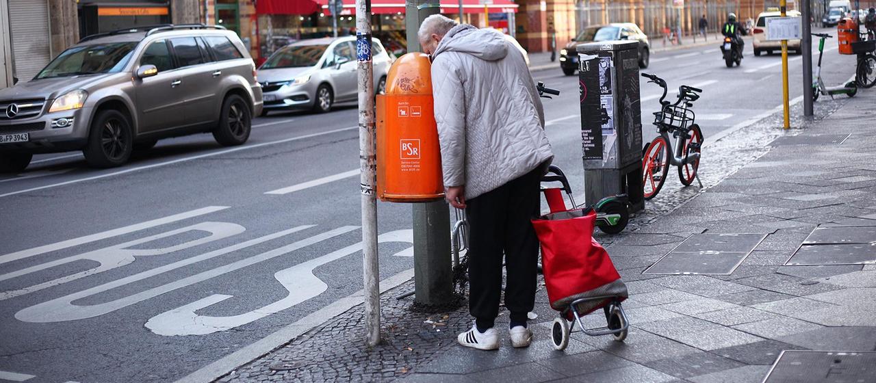 Ein Mann blickt in einen Abfalleimer und sucht nach Pfandflaschen