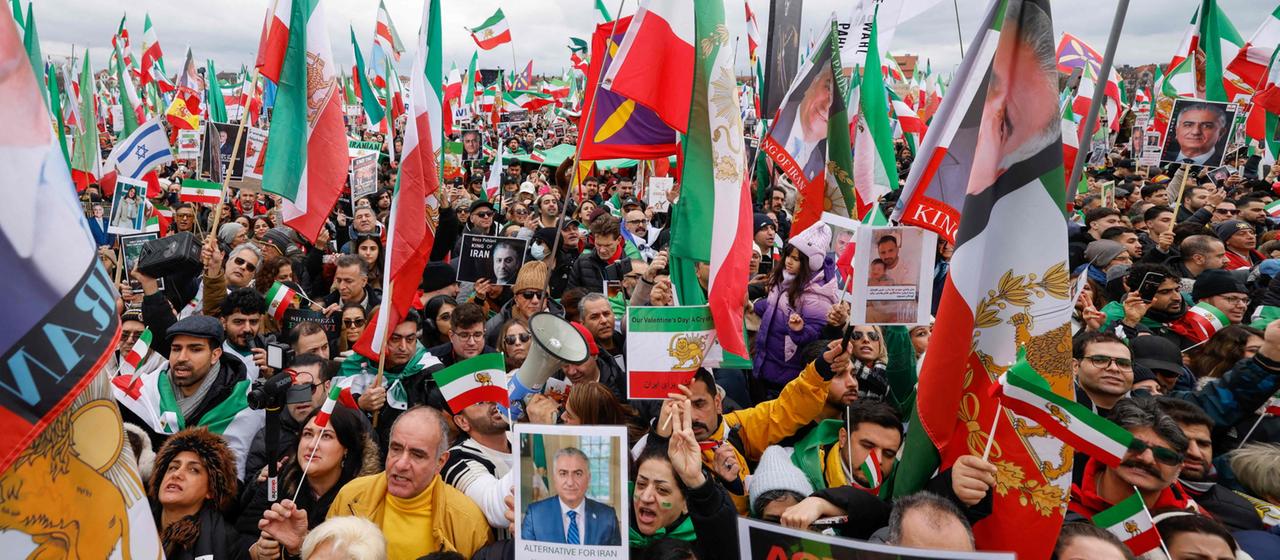 Eine große Gruppe von Menschen mit iranischen Flaggen demonstrieren und halten Plakate hoch