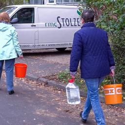 2 Frauen tragen Wasserkanister in eine großes Wohnhaus.