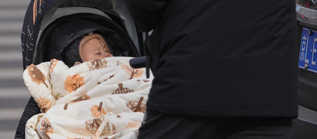 Ein Mann schiebt ein Kleinkind in einem Kinderwagen durch eine Straße. 