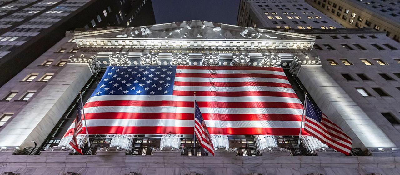 Nachtansicht der New Yorker Börse mit einer amerikanischen Flagge an der Fassade.