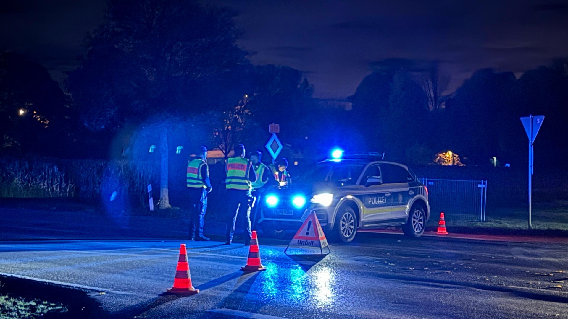 Ein Polizeiwagen mit Blaulicht auf einer nächtlichen Straße, davor zwei Einsatzkräfte mit Warnwesten. | dpa