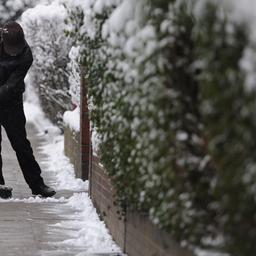 Ein Mann kehrt in Hamburg den Schnee auf einem Gehsteig.