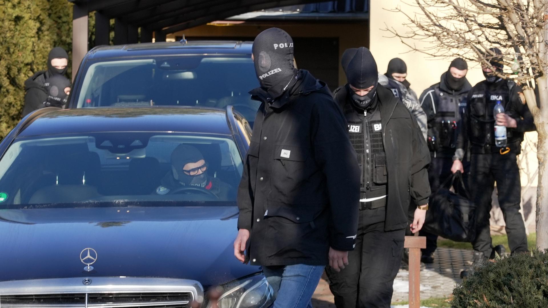 Vermummte Einsatzkräfte des Bundeskriminalamtes (BKA) gehen nach einer Durchsuchung vor einem Haus entlang. (Archivfoto: 21.01.2026) | dpa