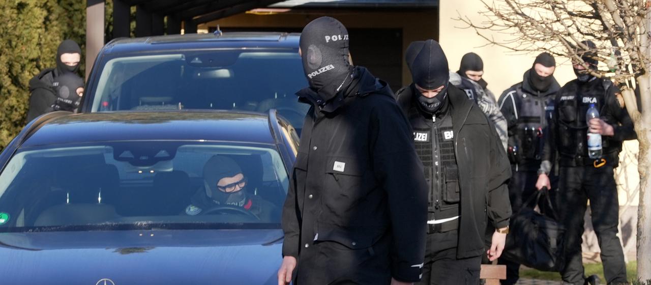 Vermummte Einsatzkräfte des Bundeskriminalamtes (BKA) gehen nach einer Durchsuchung vor einem Haus entlang. (Archivfoto: 21.01.2026)