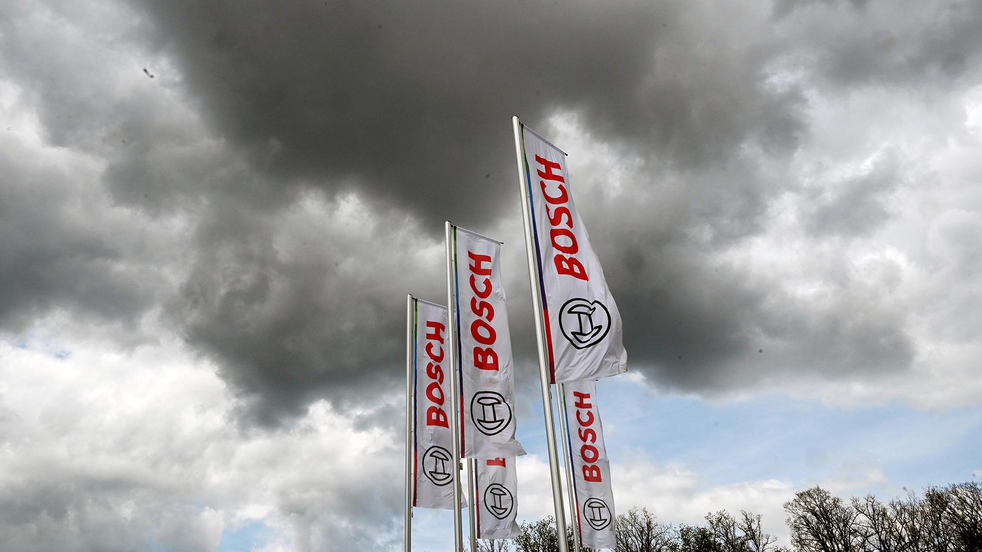 Das Logo von Bosch ist auf Fahnen am Bosch Campus vor dunklen Wolken zu sehen. | Bernd Weißbrod/dpa