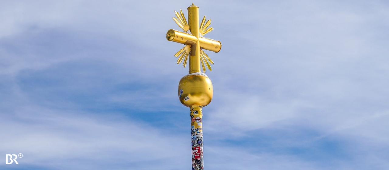 Hunderte Aufkleber auf dem vergoldeten Gipfelkreuz der Zugspitze