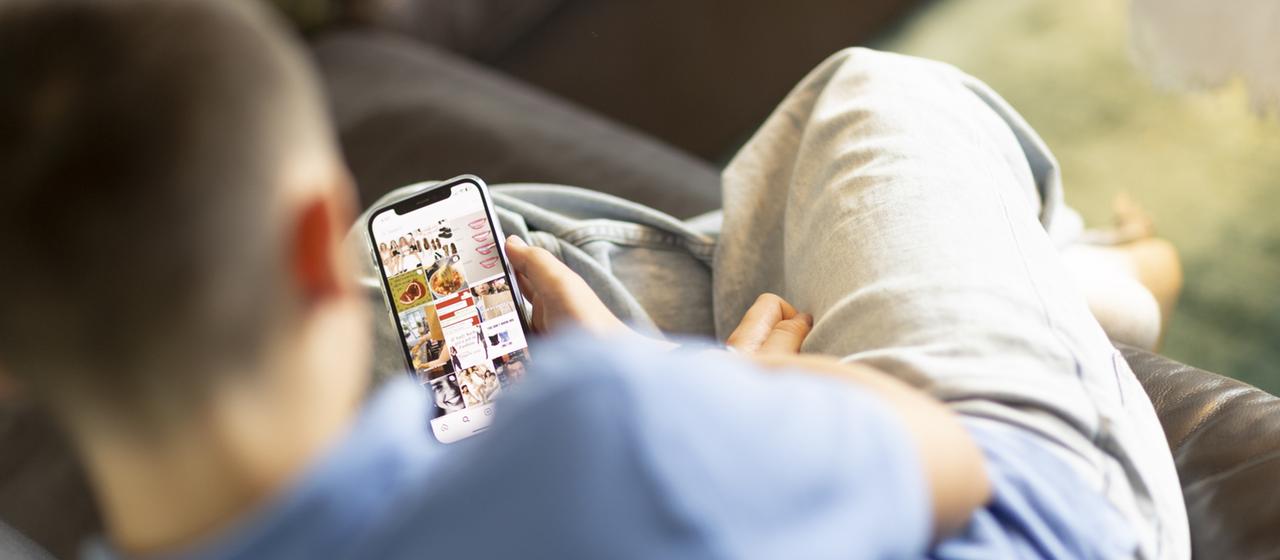 Ein Kind sitzt auf einem Sofa und schaut auf ein Handy.