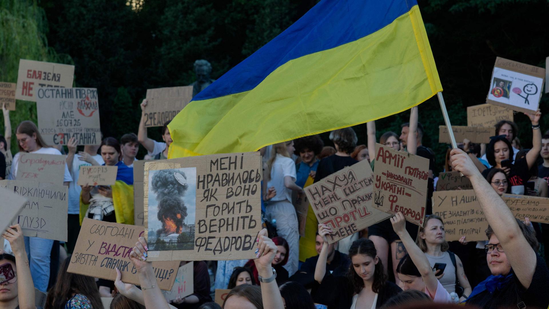 Demonstranten halten Plakate und eine Ukraine-Flagge | AFP