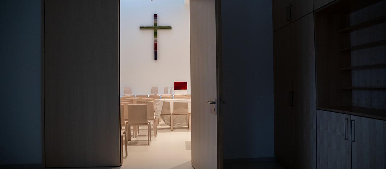 Ein Kreuz hängt im Innenraum einer Kirche an der Wand.