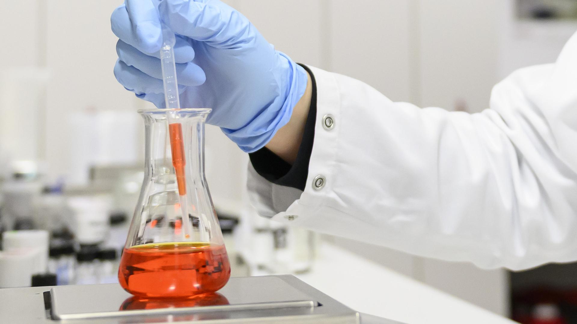 Eine Person arbeitet in einem Labor mit einem Reagenzglas | dpa