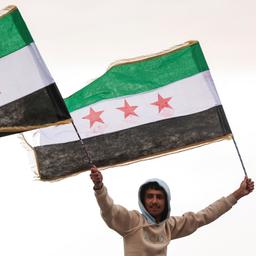 Ein Mann hält Flaggen der syrischen Rebellen in den Händen