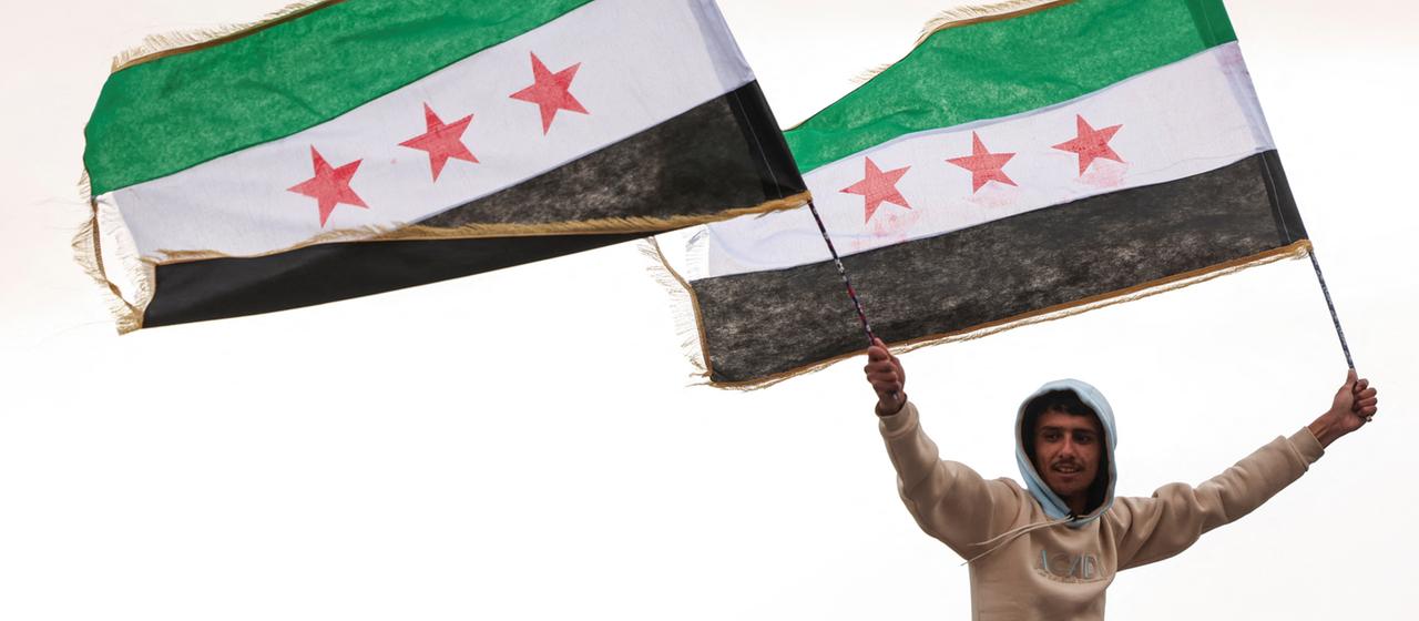 Ein Mann hält Flaggen der syrischen Rebellen in den Händen