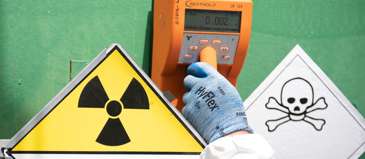 Ein Mensch hält einen Geigerzähler an einen Uran-Transportbehälter.