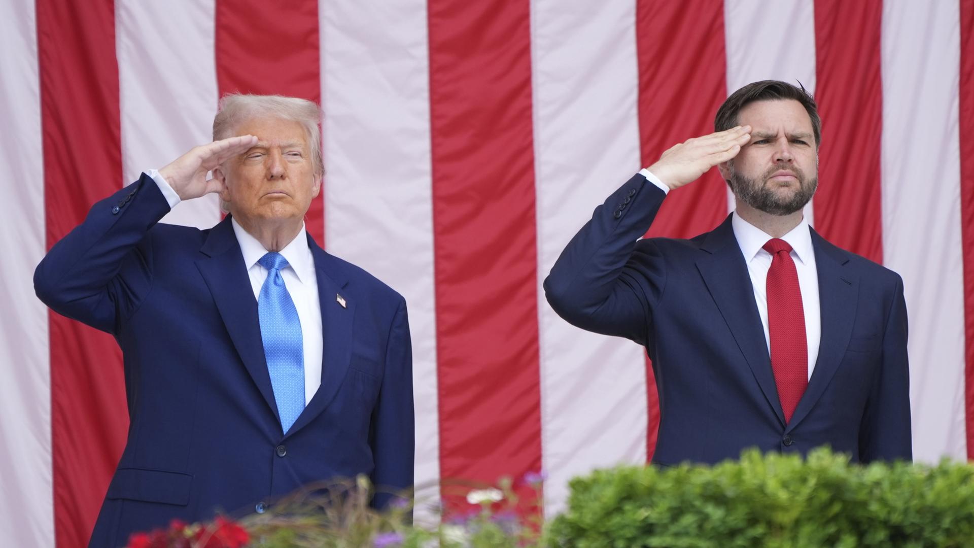 Donald Trump und JD Vance salutieren vor einer US-amerikanischen Flagge | dpa