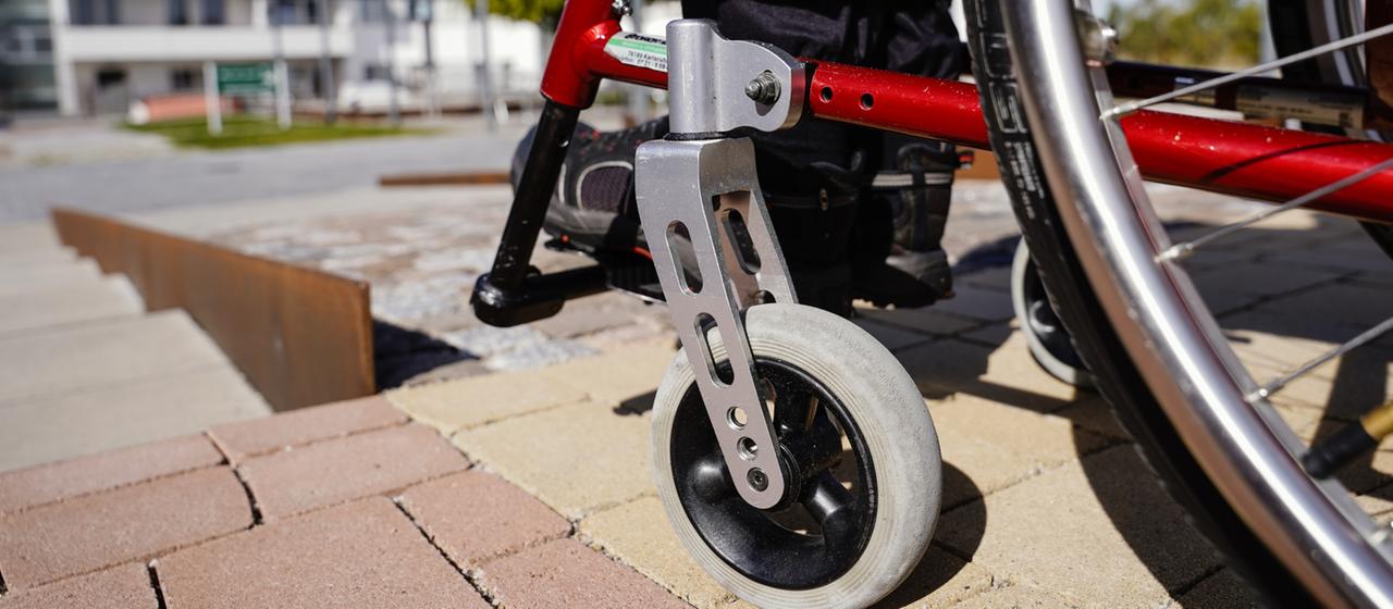 Ein Rollstuhlfahrer steht vor einem abschüssigen Weg mit Kopfsteinpflaster