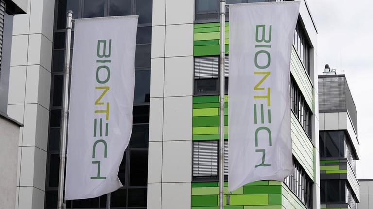Fahnen wehen vor der Firmenzentrale des Impfstoffherstellers Biontech. Das Unternehmen plant einen massiven Stellenabbau und die Schließung mehrerer Produktionsstandorte. Bei der Hauptversammlung wird es spannend.