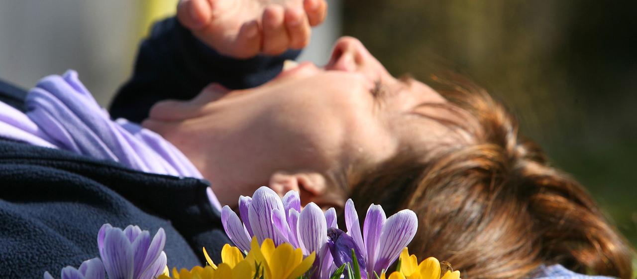 Eine Frau liegt bei Würzburg (Bayern) auf einer mit Krokussen bewachsenen Wiese und gähnt.