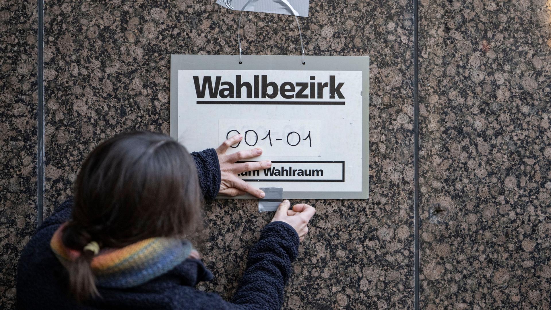 Eine Wahlhelferin befestigt ein Schild mit der Aufschrift 