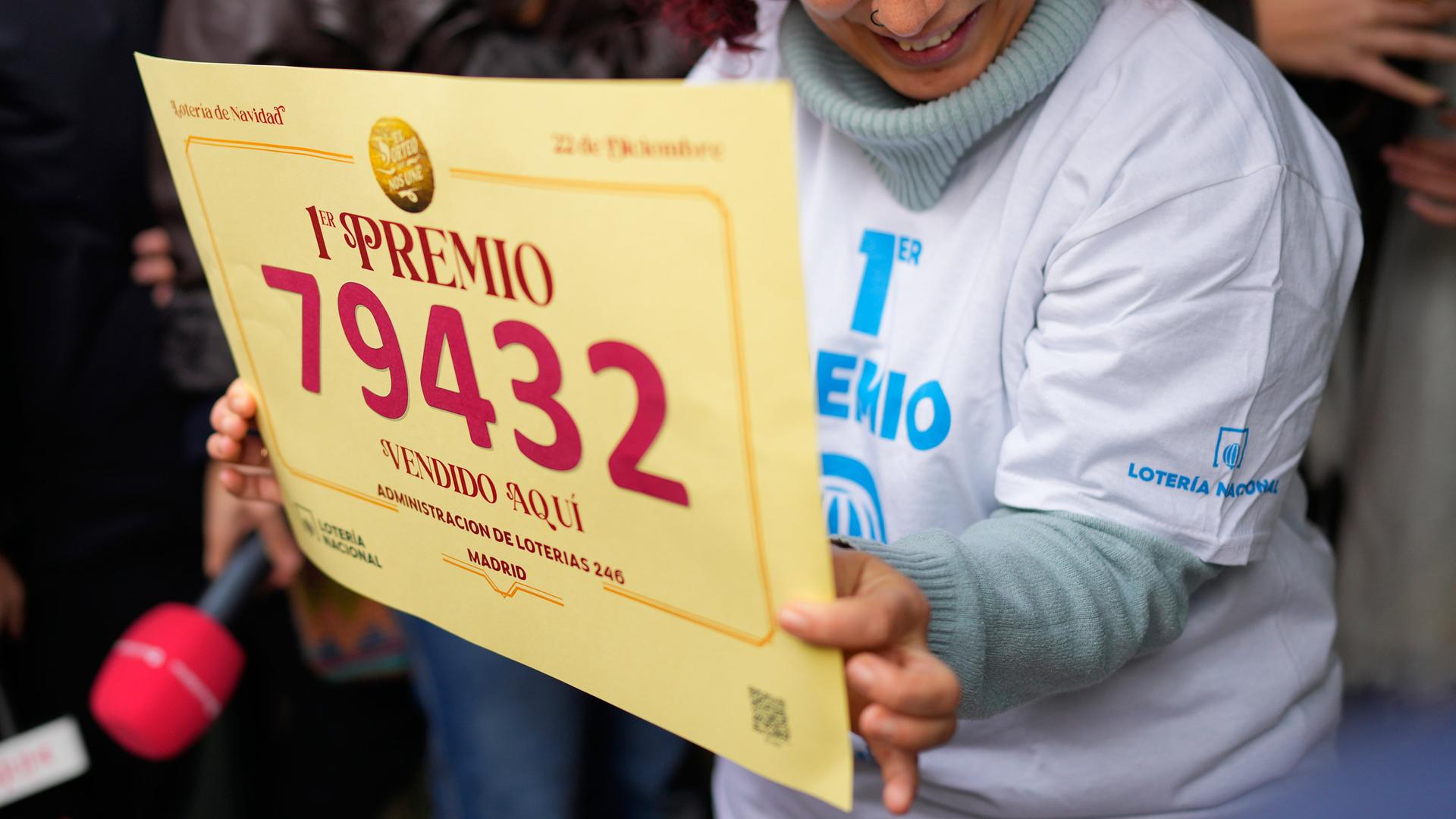 Eine Losverkäuferin hält ein Schild mit der Gewinnernummer 79.432 hoch. | AP