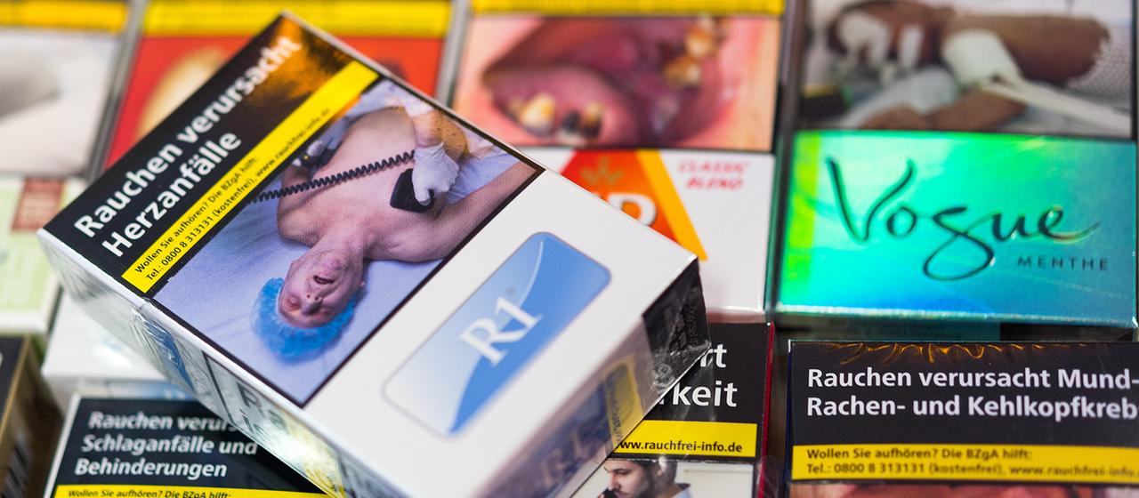 Zigarettenschachteln mit Schockbildern liegen auf einem Tresen in einem Kiosk.