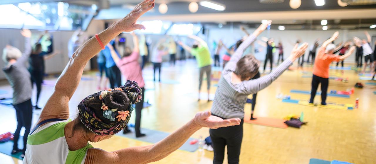 Teilnehmer eines Sportangebots für ältere Menschen beugen sich zur Seite.