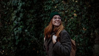 Eine lächelnde Frau geht durch einen Park.