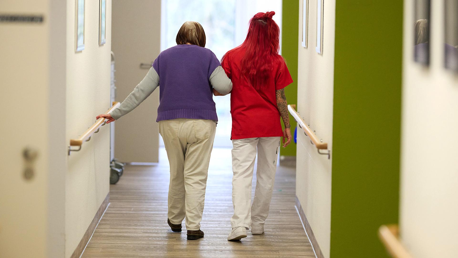 Eine Pflegekraft begleitet in einem Pflegezentrum eine Seniorin durch den Flur.  | dpa