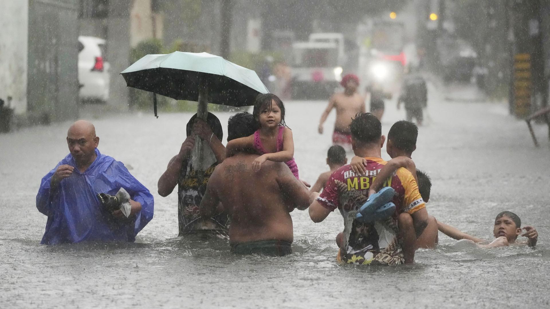 Kinder werden während eines heftigen Regengusses in einem Wohngebiet auf den Philippinen in Sicherheit gebracht. | dpa