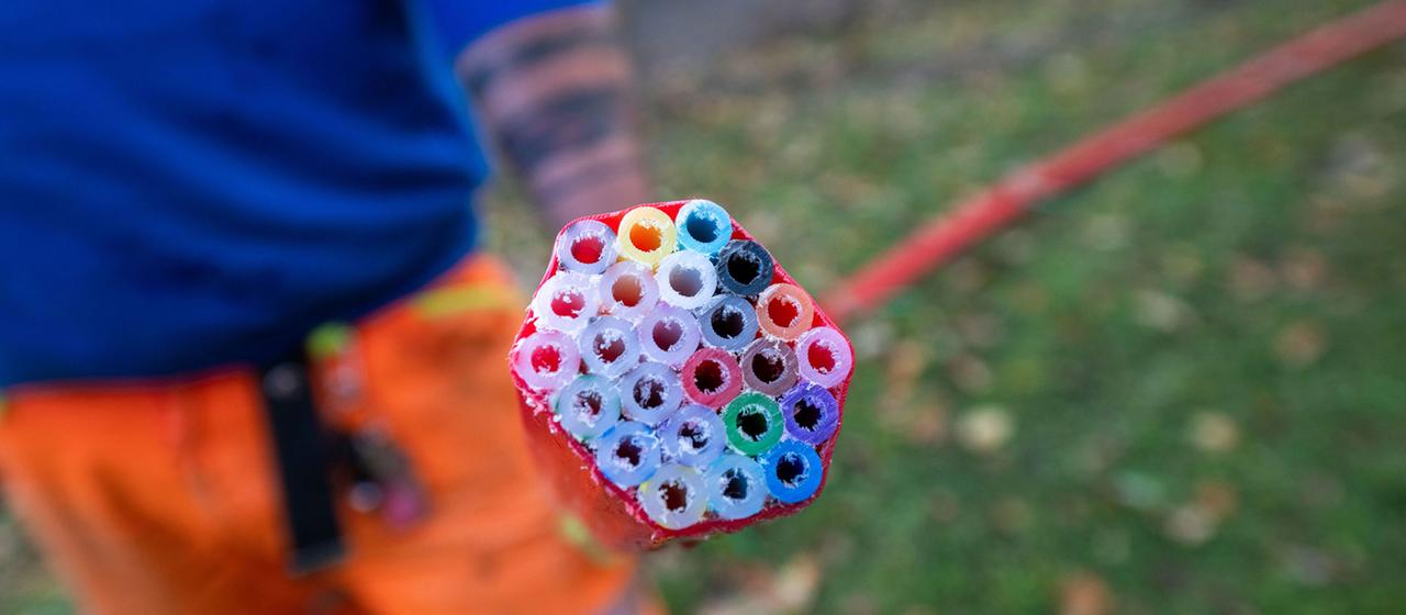 Ein Arbeiter hält ein rotes Schutzrohr mit Leerrohren für Glasfaserkabel in der Hand. 