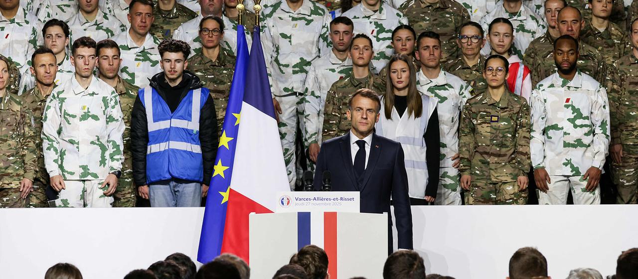Emmanuel Macron steht an einem Redepult, hinter ihm stehen Militärangehörige.