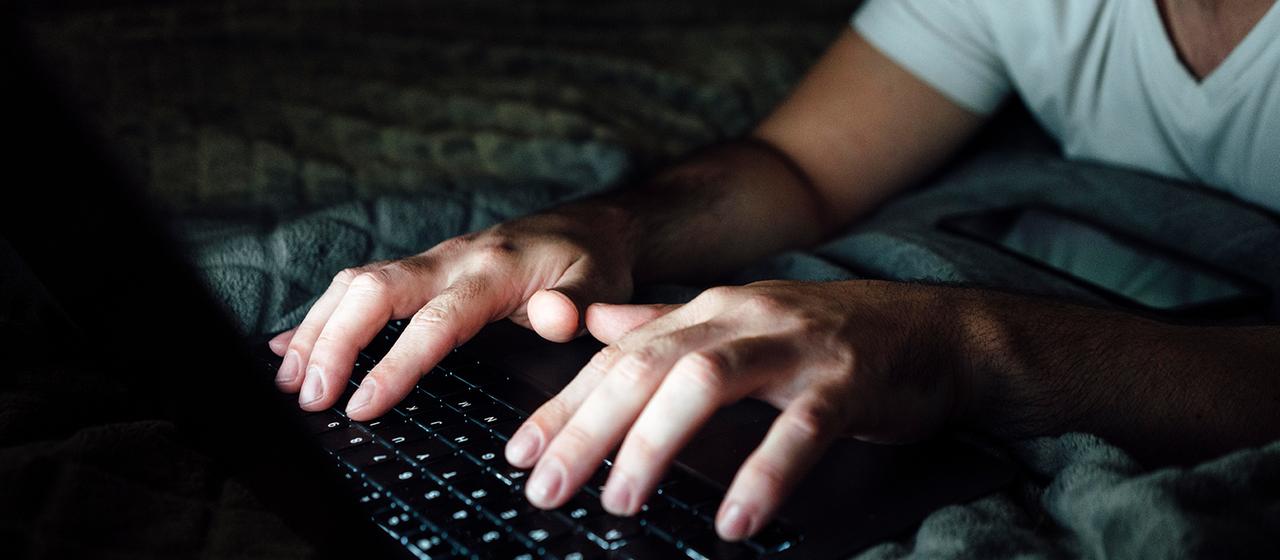 Ein Mann tippt in einem dunklen Raum auf einem Laptop.