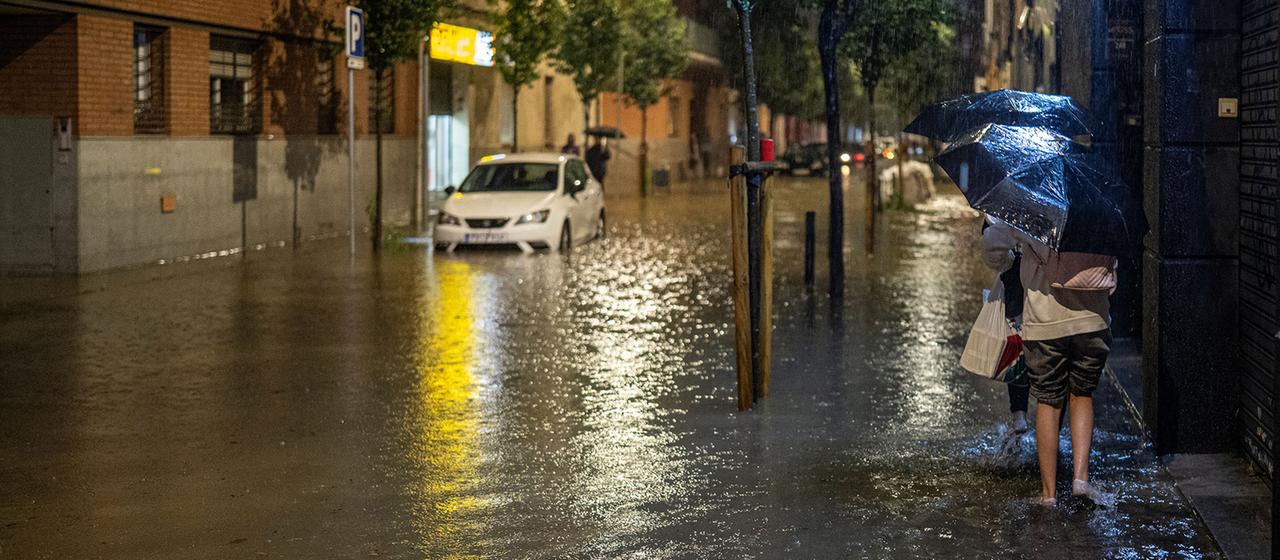 Menschen gehen an einer überfluteten Straße.