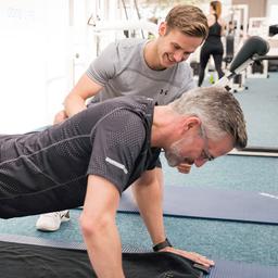 Ein Mann macht unter Anleitung Sportübungen in einem Fitnessstudio.