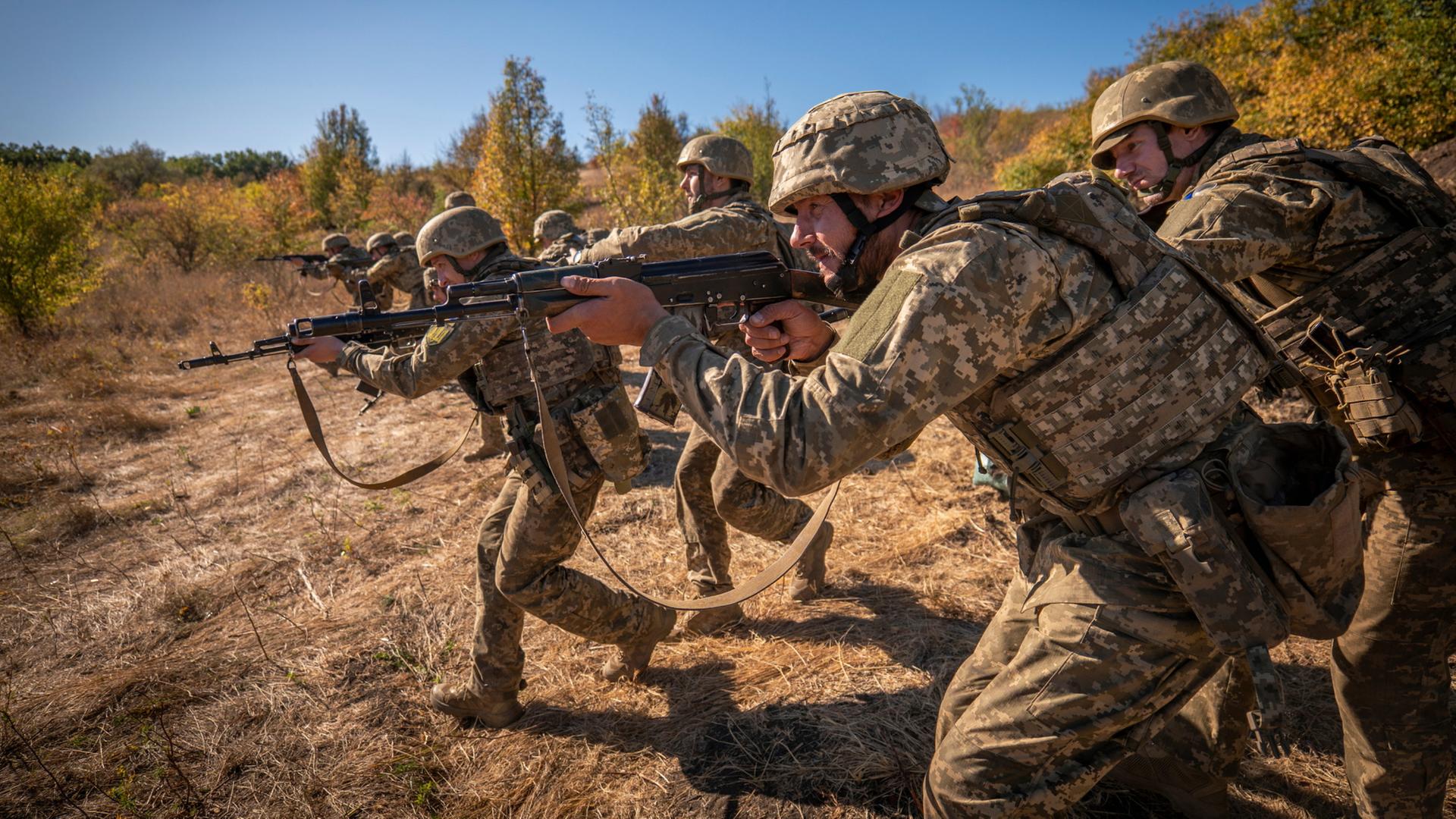 Ukrainische Soldaten gehen mit Gewehren in den Händen durch eine Landschaft. | AP