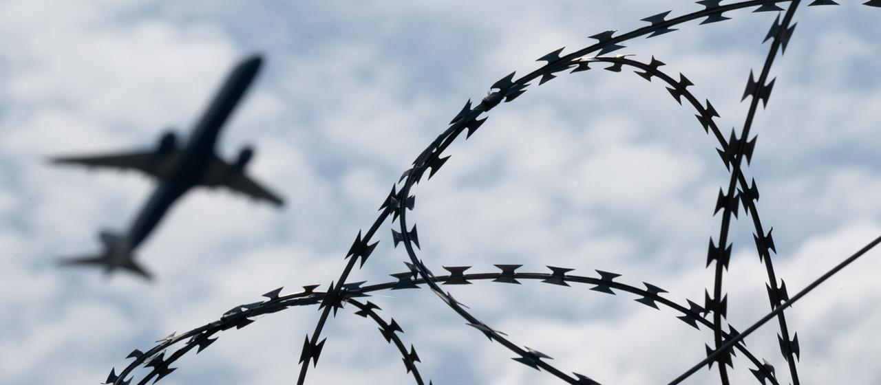 Ein Flugzeug am Himmel, davor Stacheldraht