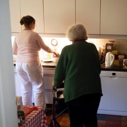 Eine jüngere Frau und eine ältere Frau mit Rollator sind in einer Küche zu sehen.