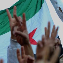 Menschen halten vor der syrischen Flagge jeweils zwei Finger in die Höhe - das Friedenszeichen.
