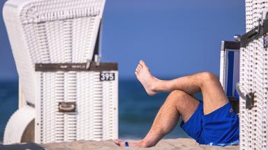 Ein Mann liegt zwischen Strandkörben am Strand.