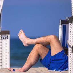 Ein Mann liegt zwischen Strandkörben am Strand.